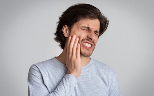 man with toothache and hand on jaw- Rhoades Family Dental